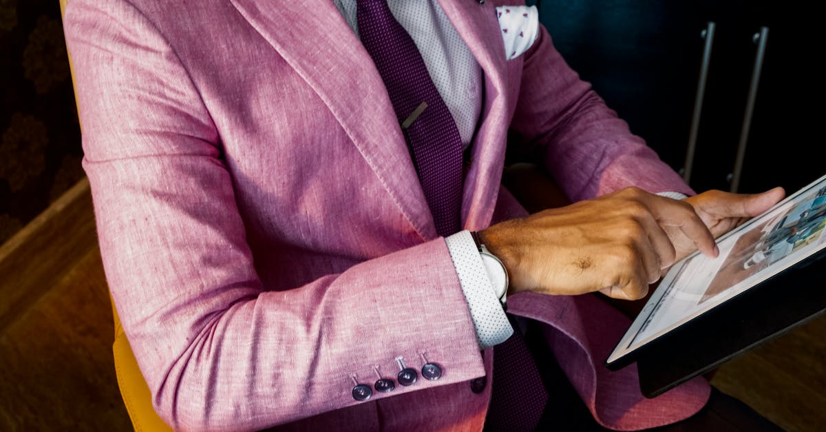 A fashionable businessman in a pink suit uses a tablet in a modern office setting.