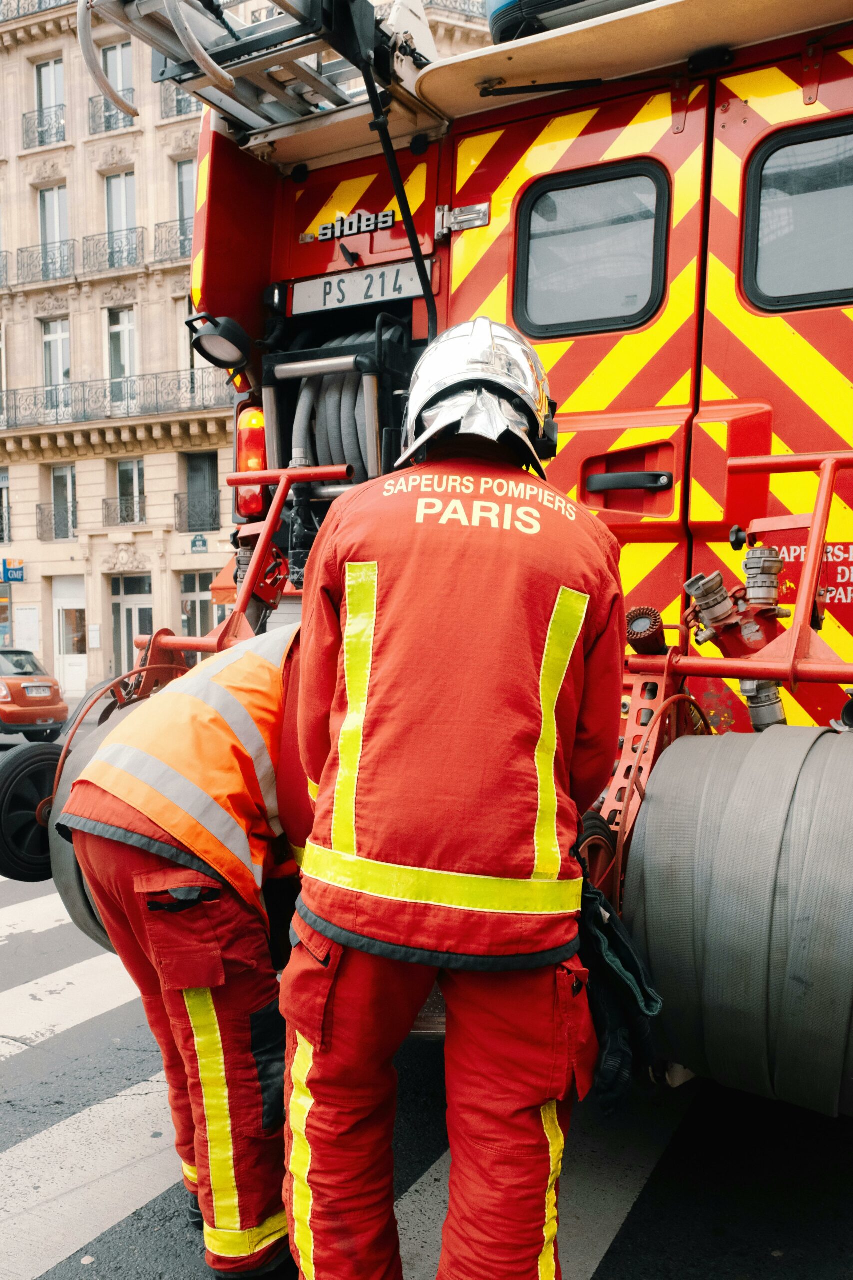 Firefighters in Paris working on a firetruck on a city street. Captured outdoors during the day.