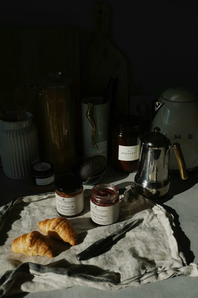 Cozy kitchen scene with croissants, jams, and a coffee pot arranged on a rustic cloth.