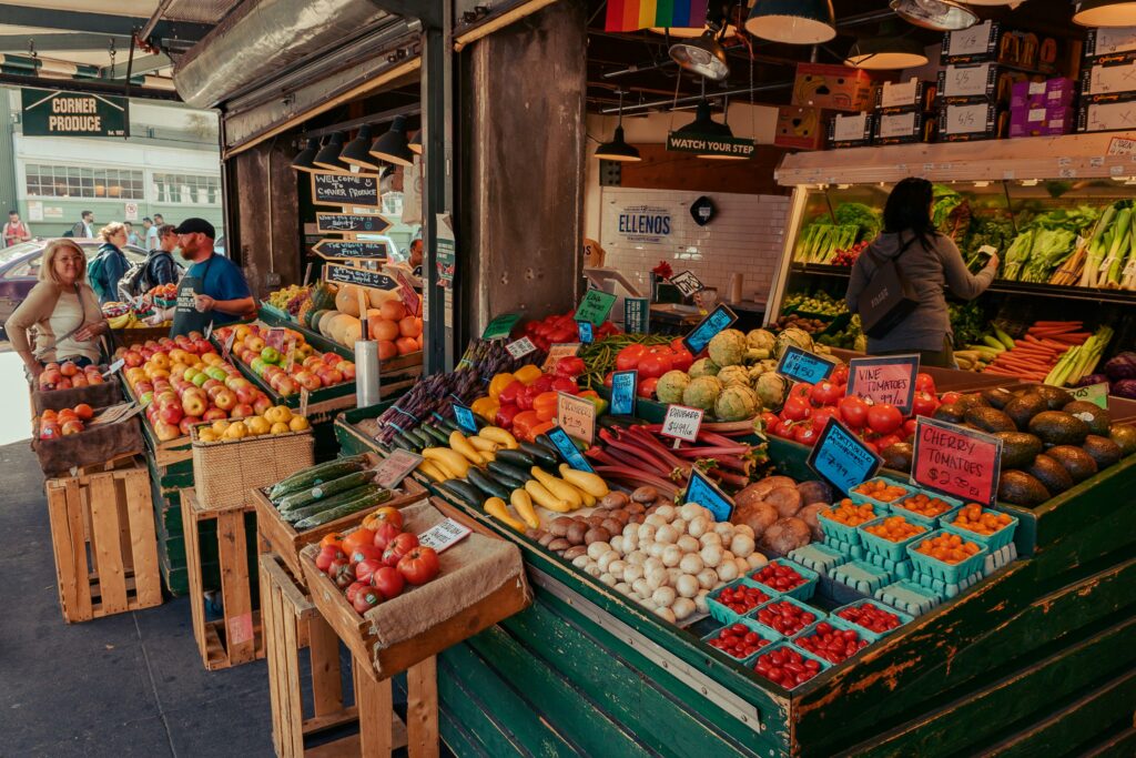 Colorful array of fresh fruits and vegetables at an outdoor farmer's market, with people browsing.