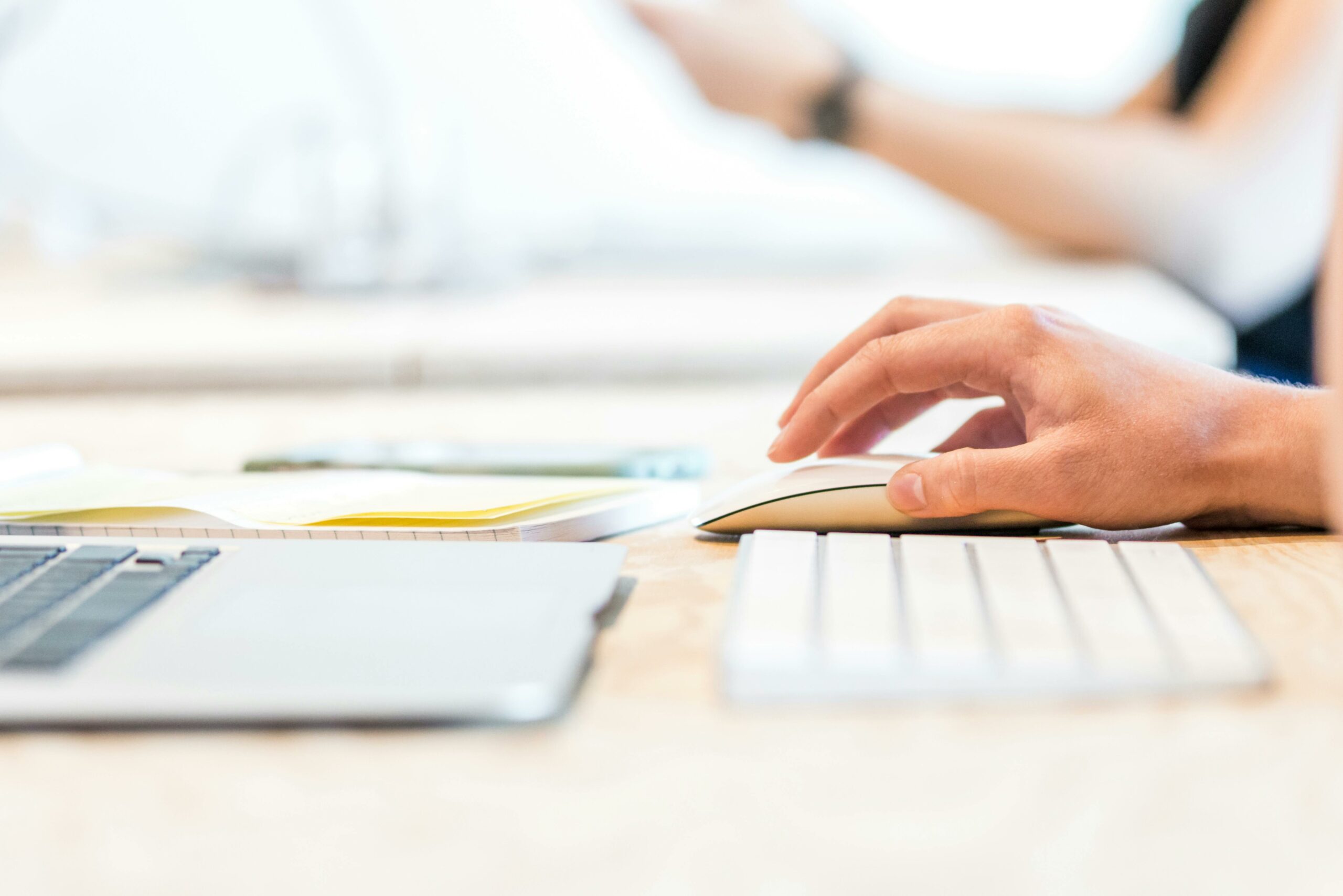 A person working at a laptop with a wireless mouse and keyboard in a bright office setting.