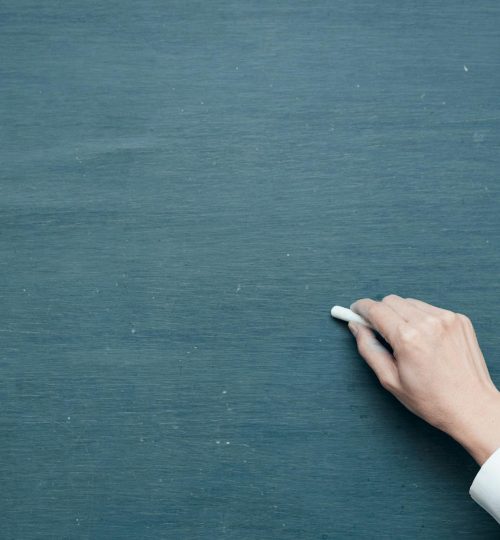 Hand holding chalk ready to write on a blank blackboard surface.