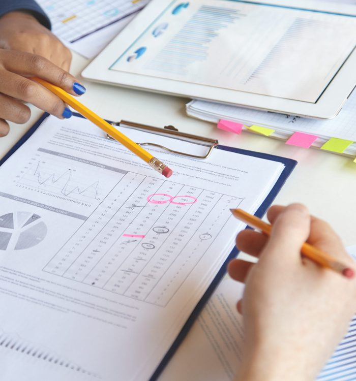 Big ideas and vision. Team of young smart people working out company strategy to reduce drawbacks. Two females discussing business plans, sitting at table with sheets of paper and electronic tablet
