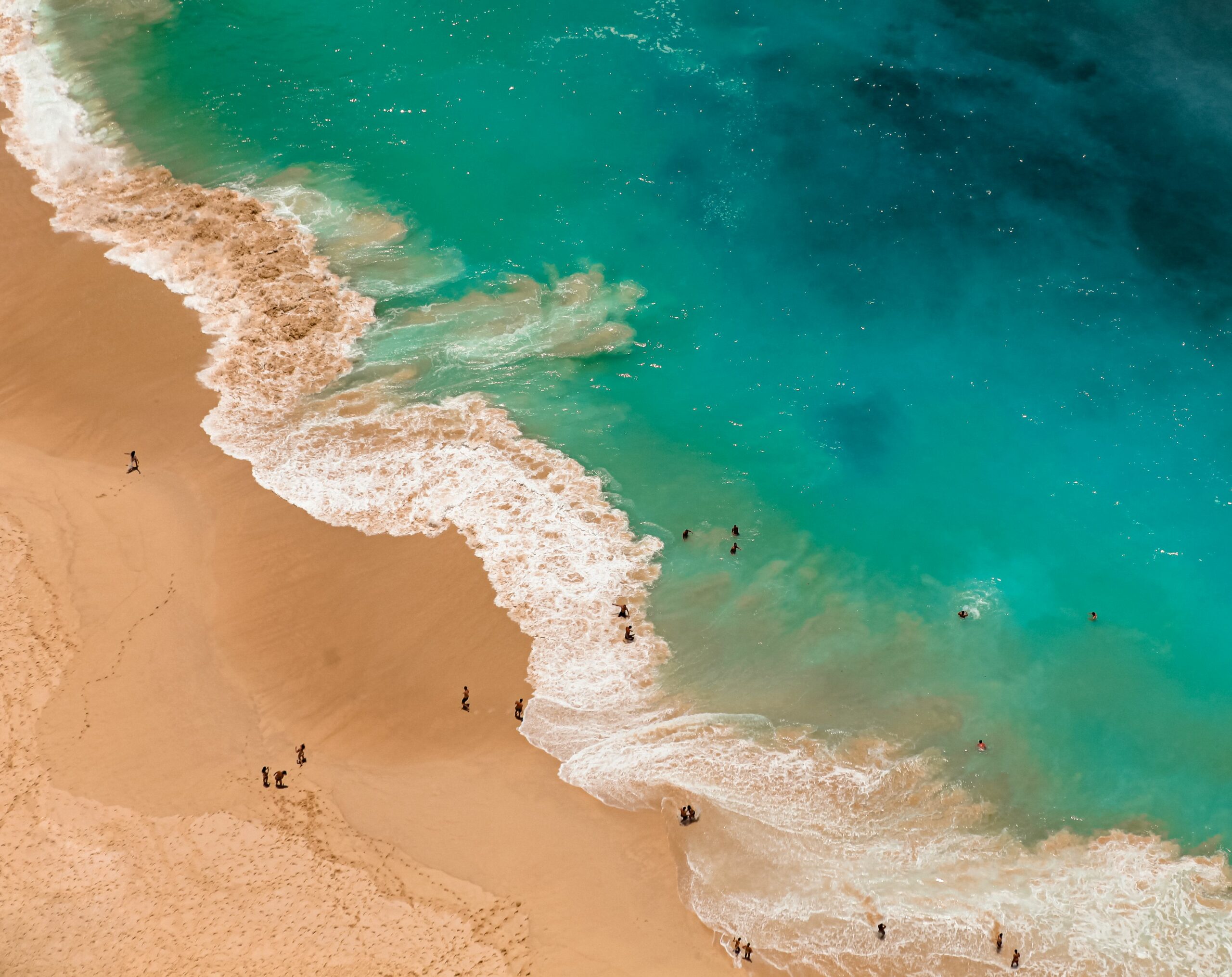A stunning aerial view of a beach with turquoise waves crashing gently on the sandy shore, people enjoying the water.