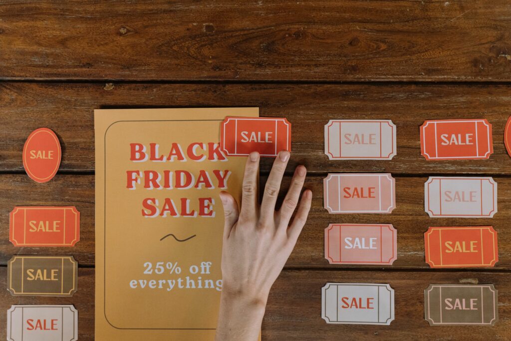 Top view of hand arranging Black Friday sale flyers on wooden table, offering 25% off everything.