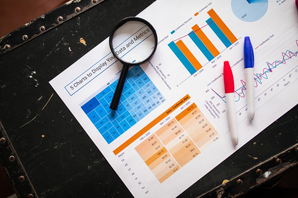 Flat lay of business charts and graphs with magnifying glass and markers on a dark surface.